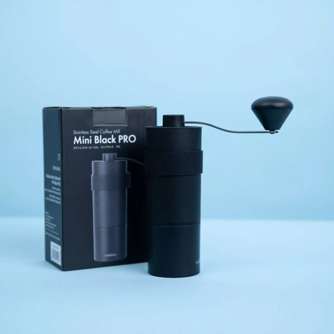Handkaffeemühle CoffeeKult Mini Black Pro aus schwarzem Metallgehäuse mit Kurbel und kompaktem, reisefreundlichem Design vor Verpackung